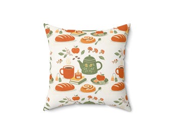 May include: Square pillow with a repeating pattern of autumnal elements. The design includes bread loaves, cinnamon rolls, apples, mushrooms, teacups, a teapot, and candles in shades of orange, green, and brown on a cream background.