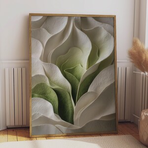 Könnte beinhalten: Ein rechteckiger Wandkunstdruck in einem hellen Holzrahmen mit einem abstrakten Design aus geschichteten, fließenden weißen und salbeigrünen papierartigen Formen mit einer strukturierten Oberfläche, die tiefe Schatten erzeugt.