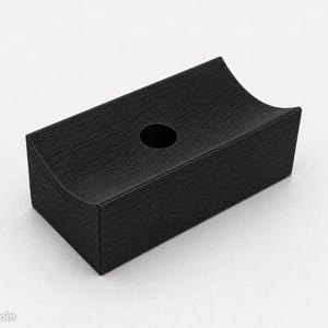 Può includere: Una maniglia per mobili rettangolare nera con finitura in metallo spazzolato. L'accessorio presenta una superficie superiore concava e un singolo foro circolare centrale per il montaggio, con un design geometrico e una texture opaca.