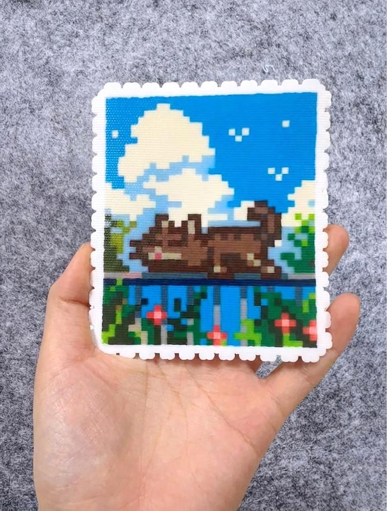 Puede incluir: Un dise&ntilde;o de arte pixelado que presenta un gato marr&oacute;n descansando sobre una repisa, sobre un cielo azul con nubes blancas. La obra de arte est&aacute; enmarcada con un borde blanco festoneado, que se asemeja a un sello. El dise&ntilde;o incluye follaje verde y flores rojas.