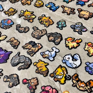 Könnte beinhalten: Eine Sammlung von Pixel-Art-Charakterfiguren in verschiedenen Farben, darunter Blau, Gelb, Braun und Lila. Die Figuren sind auf einer hellfarbigen Oberfläche angeordnet und zeigen eine Vielzahl von Designs und Formen. Die Figuren scheinen aus einem beliebten Videospiel zu stammen.