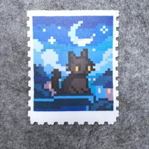 Puede incluir: Una pieza de arte pixelado que representa la silueta de un gato negro posado en un tejado bajo una luna creciente y un cielo estrellado. La obra est&aacute; enmarcada con un borde blanco similar a un sello postal. La paleta de colores incluye tonos azules, negros y amarillos.