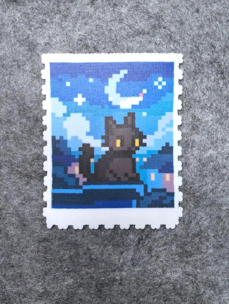 Puede incluir: Una pieza de arte pixelado que representa la silueta de un gato negro posado en un tejado bajo una luna creciente y un cielo estrellado. La obra est&aacute; enmarcada con un borde blanco similar a un sello postal. La paleta de colores incluye tonos azules, negros y amarillos.