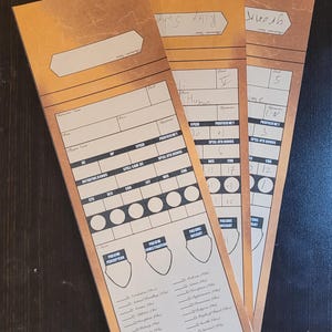 May include: Three tan character sheets for a role-playing game, with brown borders. They feature sections for stats, skills, and abilities. Each sheet has a name at the top, with handwritten details. Measurements are not applicable.