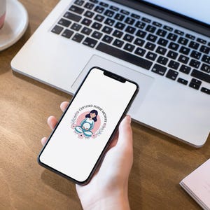 May include: A smartphone screen shows a logo with the text "CERTIFIED NURSE MIDWIFE SERVICE" within a floral wreath. The phone is held in a hand, with a laptop, a notepad, and a pen on a wooden surface.