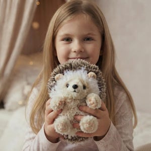 Puede incluir: Un peluche de erizo con cara y vientre de color crema suave y almohadillas de color rosa claro. La espalda está cubierta de piel sintética texturizada en tonos marrón y blanco que imita púas. Tiene orejas pequeñas, ojos oscuros y nariz negra.