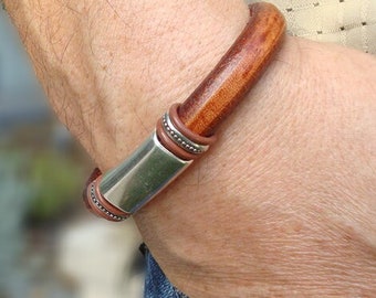 May include: A brown leather bracelet with a silver metal clasp. The bracelet is worn on a person's wrist.