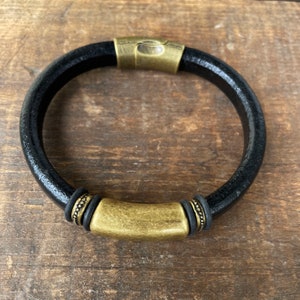 Pu&ograve; includere: Un braccialetto in pelle nera con una chiusura in metallo dorato e dettagli decorativi.