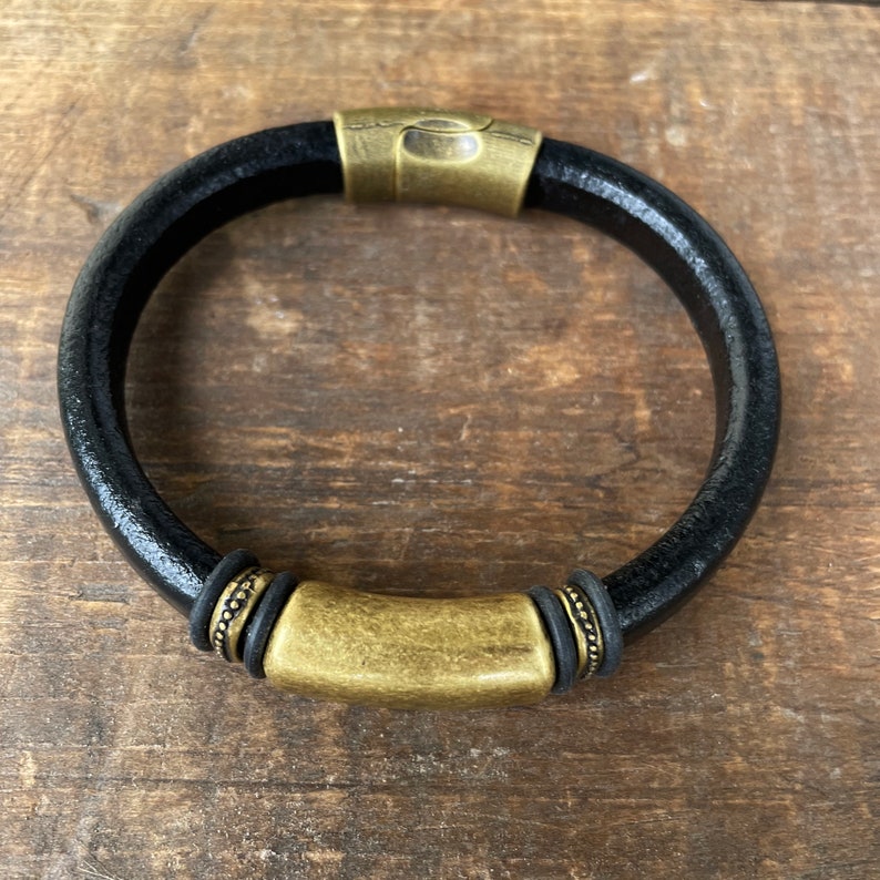 Pu&ograve; includere: Un braccialetto in pelle nera con una chiusura in metallo dorato e dettagli decorativi.