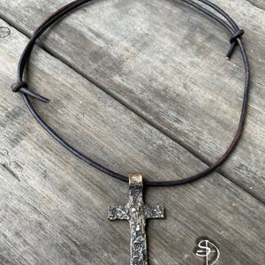 May include: A silver cross pendant with a textured surface hangs from a brown leather cord necklace.