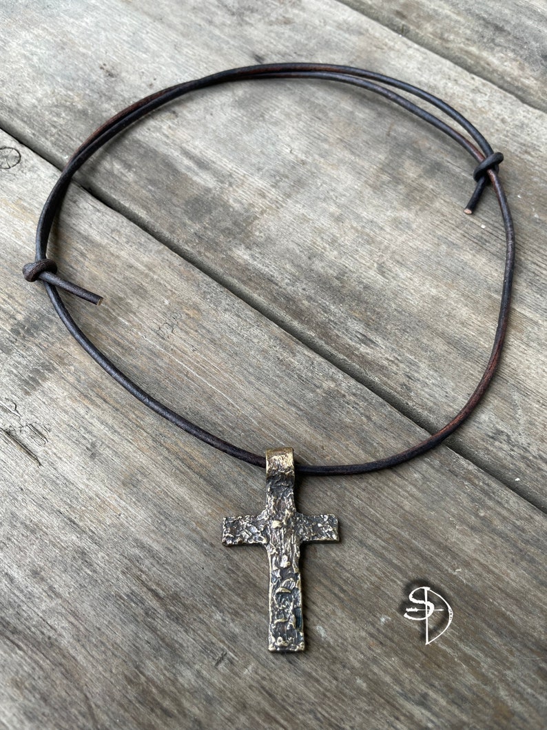 May include: A silver cross pendant with a textured surface hangs from a brown leather cord necklace.