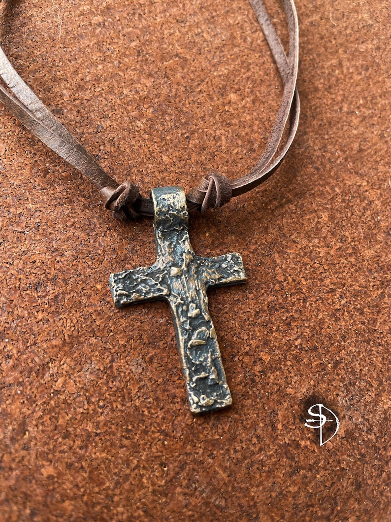 May include: A silver cross pendant with a textured surface hangs from a brown leather cord necklace.