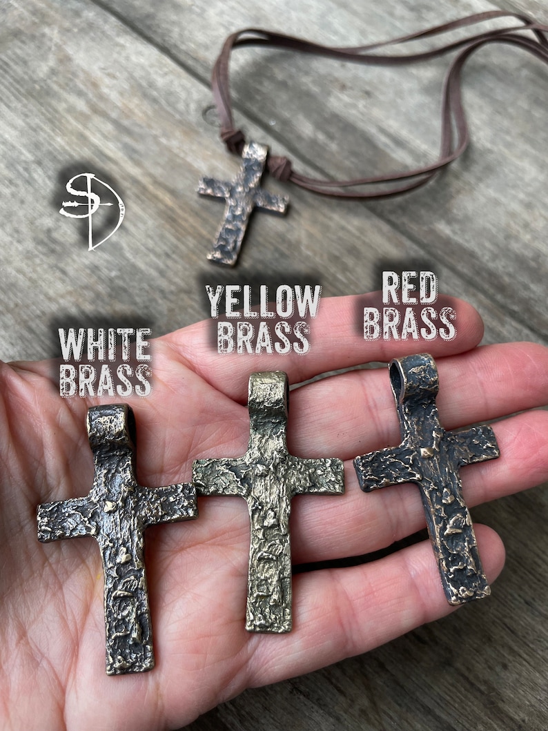 May include: Three metal cross pendants in different finishes: white brass, yellow brass, and red brass. Each cross has a textured surface and a loop at the top for hanging.