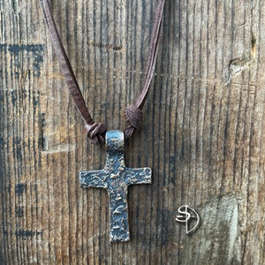 May include: A brown leather cord necklace with a textured bronze cross pendant.