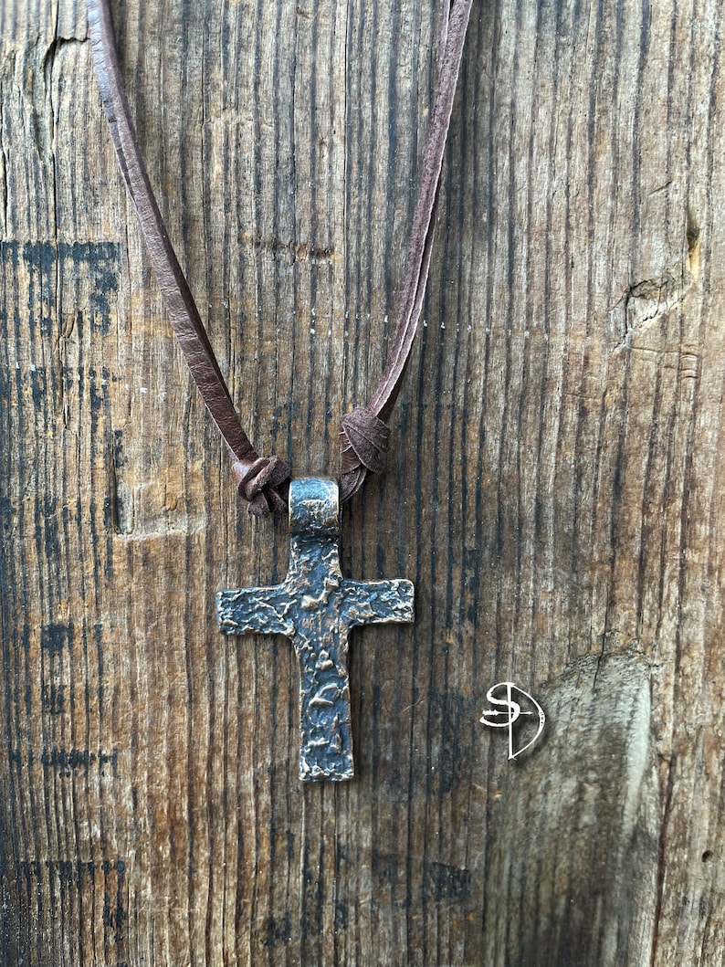 May include: A brown leather cord necklace with a textured bronze cross pendant.
