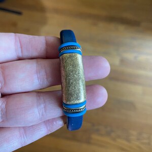 Pu&ograve; includere: Un braccialetto in pelle blu con una barra in metallo dorata e dettagli blu.