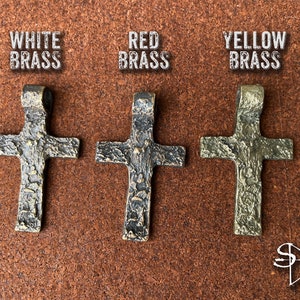 May include: Three ornate cross pendants in different finishes: white brass, red brass, and yellow brass. Each cross has a textured surface and a loop at the top for hanging.