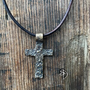 May include: A bronze cross pendant necklace with a textured surface, hanging from a brown leather cord.