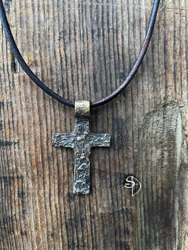 May include: A bronze cross pendant necklace with a textured surface, hanging from a brown leather cord.