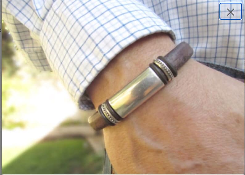 Pu&ograve; includere: Un braccialetto in pelle marrone con un ciondolo rettangolare argentato e anelli decorativi in argento.
