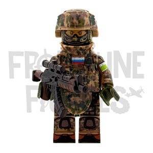 以下が含まれることがあります： 迷彩服を着た兵士の精巧なミニチュアフィギュア。ヘルメット、タクティカルベスト、スコープ付きライフルが付属。ロシア国旗のパッチと緑と白のアームバンドが付いています。全体的なデザインは軍事的なテーマを示唆しています。