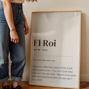 以下が含まれることがあります： 「El Roi」という言葉が大きく暗い文字で書かれた額入りのプリント。その下には「私を見る神」という定義があります。プリントは明るい木製のフレームに入っています。