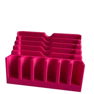 Può includere: Un organizzatore di monete rosa acceso con fessure per diverse denominazioni. L'organizzatore ha fessure etichettate per monete da 5c, 10c, 25c, 50c e 1€. Il portamonete è realizzato in plastica.