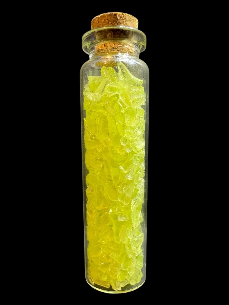 K&ouml;nnte beinhalten: Ein kleines, klares Glasfl&auml;schchen mit zahlreichen hellgelb-gr&uuml;nen, fragmentierten St&uuml;cken. Die Flasche ist mit einem Korken verschlossen. Der Hintergrund ist schwarz und hebt den Inhalt der Flasche hervor.