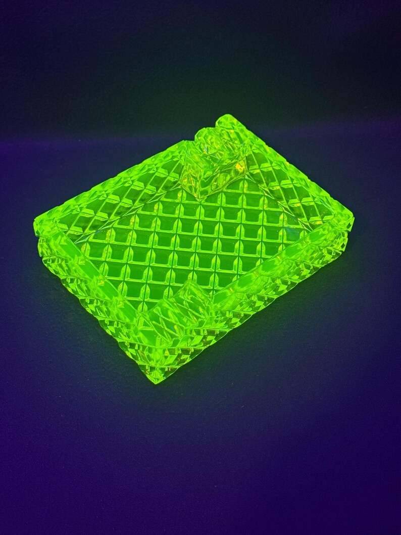 May include: A neon green, rectangular ashtray with a diamond pattern. The ashtray has a small, raised area for resting cigarettes. The glass ashtray is a vibrant, eye-catching piece.