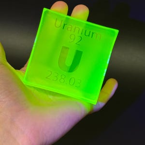 Può includere: Una piastrella quadrata in acrilico verde lime fluorescente che riporta le informazioni dell'elemento Uranio della tavola periodica. Il testo include la parola Uranium, il numero atomico 92, il simbolo U e la massa atomica 238,03, incisi in un carattere chiaro.