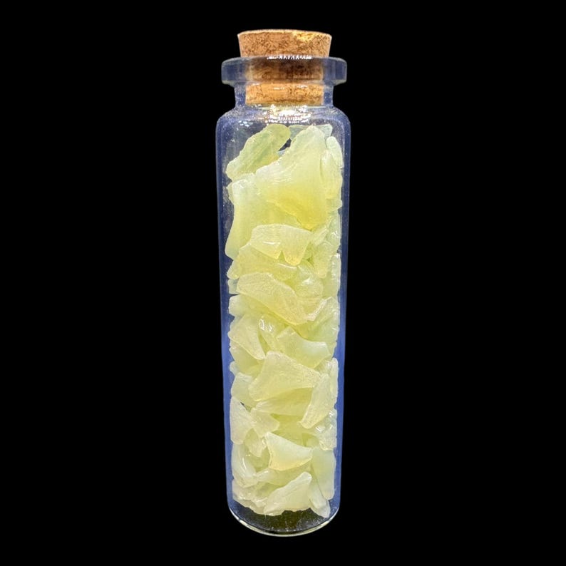 K&ouml;nnte beinhalten: Eine kleine, transparente Glasflasche gef&uuml;llt mit hellgelben, unregelm&auml;&szlig;ig geformten Fragmenten. Die Flasche hat einen Korkenverschluss. Die Fragmente scheinen eine Art Kristall oder Mineral zu sein.