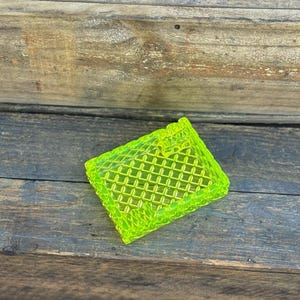 May include: A neon green, rectangular, decorative tray with a diamond pattern. The tray is made of a translucent material and sits on a weathered wooden surface.