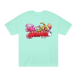Puede incluir: Camiseta azul claro con un diseño gráfico colorido. El diseño incluye la palabra "WaWa" en rojo y amarillo, junto con elementos de dibujos animados como una criatura rosa, una mano verde y un ojo.
