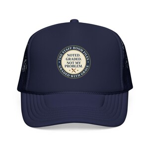 May include: A navy blue trucker cap with a mesh back and a circular patch on the front. The patch features the text "THE STAFF ROOM FILES" and "GRADED WITH GRACE" surrounding the words "NOTED. GRADED. NOT MY PROBLEM." with two crossed pencils.