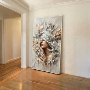 May include: A large, vertical canvas art piece featuring a woman with a blindfold, surrounded by sculpted doves and floral elements. The artwork uses a palette of white, beige, and peach tones, creating a textured, three-dimensional effect.