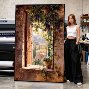 May include: Large framed artwork depicting a Tuscan landscape scene. The painting shows a window with a view of vineyards, cypress trees, and a stone building. Grapes and vines frame the window. The artwork is in a black frame.