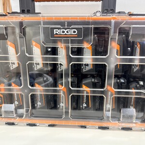 May include: A clear plastic and black Ridgid tool case with orange trim, filled with multiple black and orange 18V and 4Ah batteries. The case has a handle and is divided into compartments.