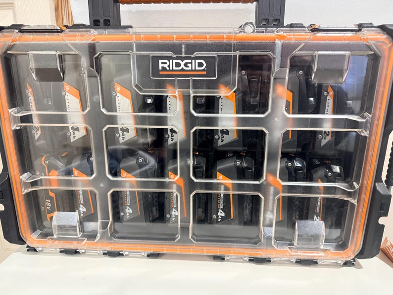 May include: A clear plastic and black Ridgid tool case with orange trim, filled with multiple black and orange 18V and 4Ah batteries. The case has a handle and is divided into compartments.