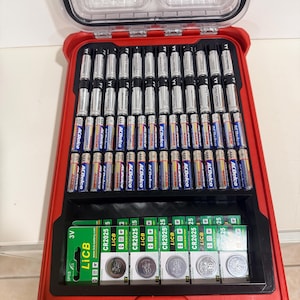 May include: A red storage case filled with various batteries. The case contains AA and AAA batteries, along with several CR2025 lithium coin cell batteries. The batteries are neatly organized within the case.