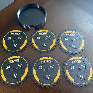 May include: A set of six black and yellow RIDGID circular saw blades with a black holder. Each blade has the text "RIDGID", "24", "7 1/4", and "5/8" printed on it. The blades are designed for cutting wood.