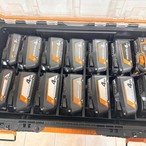 May include: A black and orange tool case filled with multiple black and gray rechargeable power tool batteries. The batteries are labeled with their voltage and amp-hour ratings, including 2Ah and 4Ah, and 18V. The case has an orange handle and a clear lid.