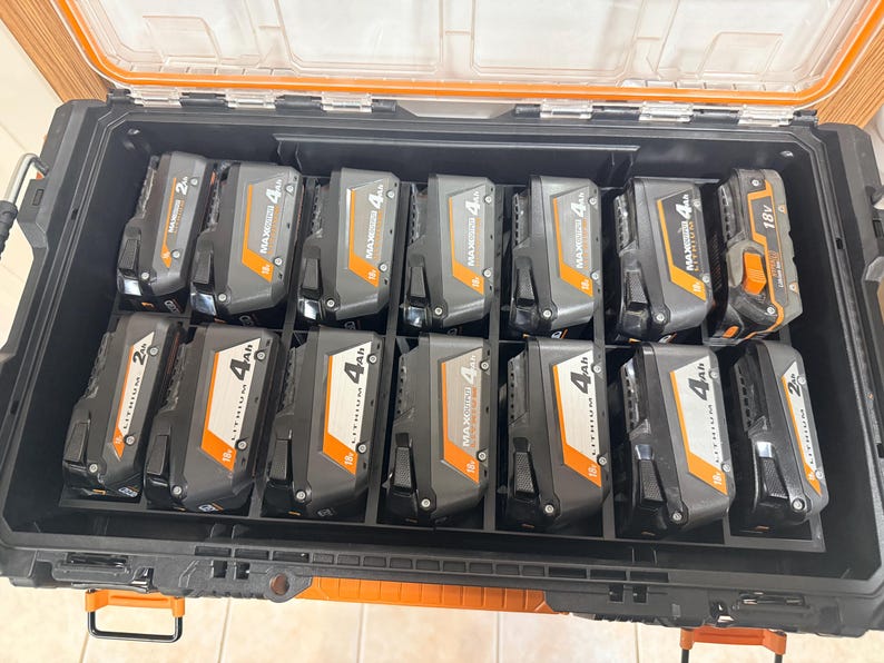 May include: A black and orange tool case filled with multiple black and gray rechargeable power tool batteries. The batteries are labeled with their voltage and amp-hour ratings, including 2Ah and 4Ah, and 18V. The case has an orange handle and a clear lid.