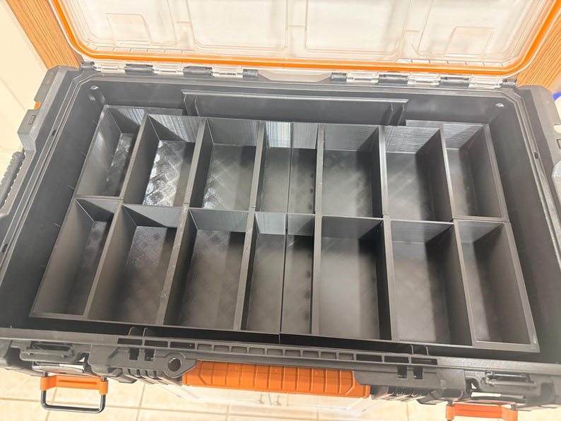 May include: Open black toolbox with an orange handle and clear lid. The interior is divided into multiple compartments of varying sizes. The toolbox is designed for organizing and storing tools and other small items. The lid is open, revealing the interior organization.