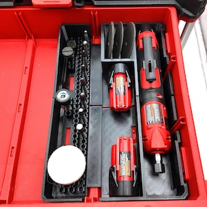 May include: A red and black plastic tool organizer tray containing a cordless rotary tool, two red battery packs, three circular cutting discs, and a row of various metal burr bits and a white circular polishing pad arranged in custom slots.
