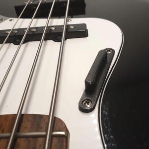Könnte beinhalten: Nahaufnahme einer schwarz-weißen E-Bassgitarre. Der Bass hat vier Saiten, ein weißes Schlagbrett und einen schwarzen Korpus. Kopfplatte und Stimmwirbel sind im Bild nicht zu sehen.