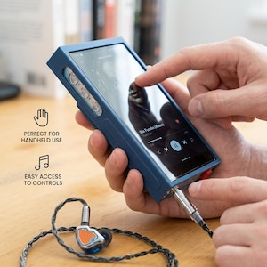 Op de afbeelding: Een blauwe draagbare digitale audiospeler met een touchscreen waarop een muziekinterface wordt weergegeven. Het apparaat heeft zilveren knoppen en een rode poort. In-ear oortelefoons met een zilver en oranje ontwerp zijn aangesloten.