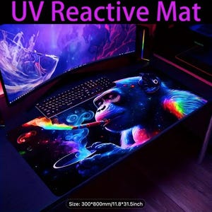Puede incluir: Alfombrilla de juego reactiva a los rayos UV con una colorida ilustración de un gorila fumando un cigarro, con una estela de humo de arcoíris. La alfombrilla es negra con un fondo temático de galaxia y mide 300mm x 800mm.