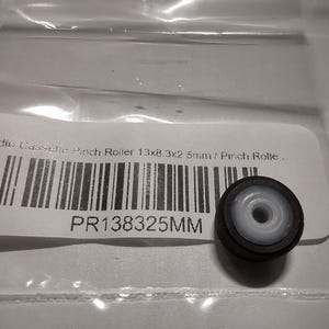 Może przedstawiać: Czarny i biały wałek dociskowy do odtwarzaczy kaset audio. Rolka ma wymiary 13x8,3x2,5mm i ma biały środek. Produkt jest zapakowany w przezroczystą plastikową torbę z etykietą zawierającą kod kreskowy i kod produktu PR138325MM.
