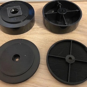 May include: Four black plastic furniture feet components. Two are cylindrical with a central hole and a square insert. The other two are circular, one with a central hole and concentric ridges, the other with a cross-shaped support.