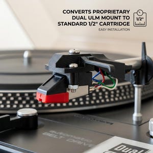 May include: A close-up of a black and silver turntable cartridge mount with red detailing. The text reads "CONVERTS PROPRIETARY DUAL ULM MOUNT TO STANDARD 1/2" CARTRIDGE EASY INSTALLATION". The turntable is black with silver details.